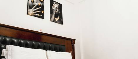 A hotel room with a wooden headboard, white bedding, and two black-and-white artwork pieces on the wall.