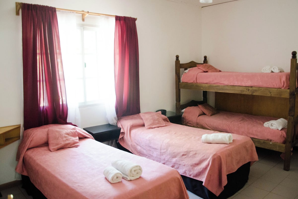 Une chambre de dortoir avec deux lits simples, un lit superposé et un bureau.