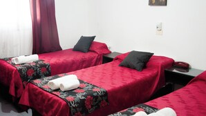 A hotel room with two single beds, each with a red bedspread and a black floral pillow. There is a small table between the beds with a telephone and a power outlet. - Almeria Hotel (San Rafael)