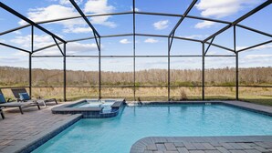 Una piscina con cerramiento de vidrio, sillas de descanso y vistas a un bosque.