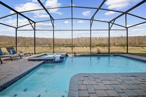 Ein Schwimmbad mit Glasveranda, Liegestühlen und Blick auf einen Wald.