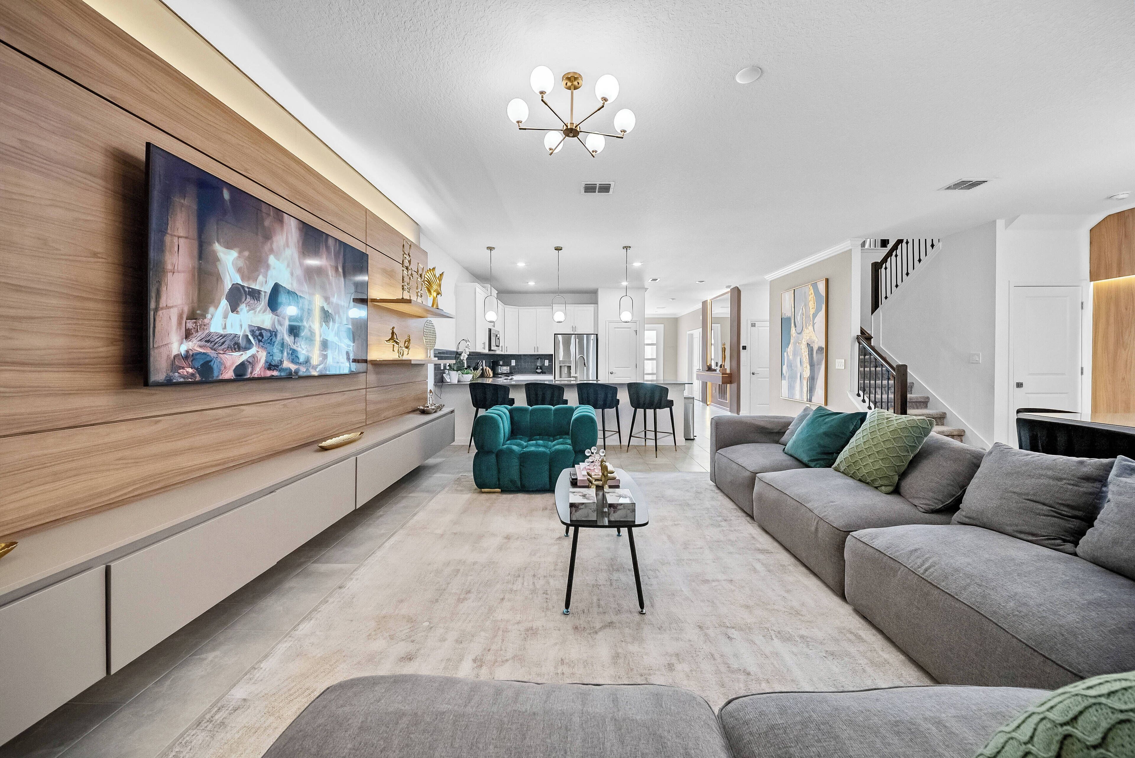A modern living room with a large flat-screen TV, a teal sofa, a grey sectional, and a coffee table.