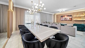 Una sala de estar moderna con una gran mesa de comedor, sillas negras, un sofá gris y un televisor en la pared.