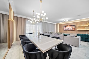 Ein modernes Wohnzimmer mit großem Esstisch, schwarzen Stühlen, einem grauen Sofa und einem Fernseher an der Wand.