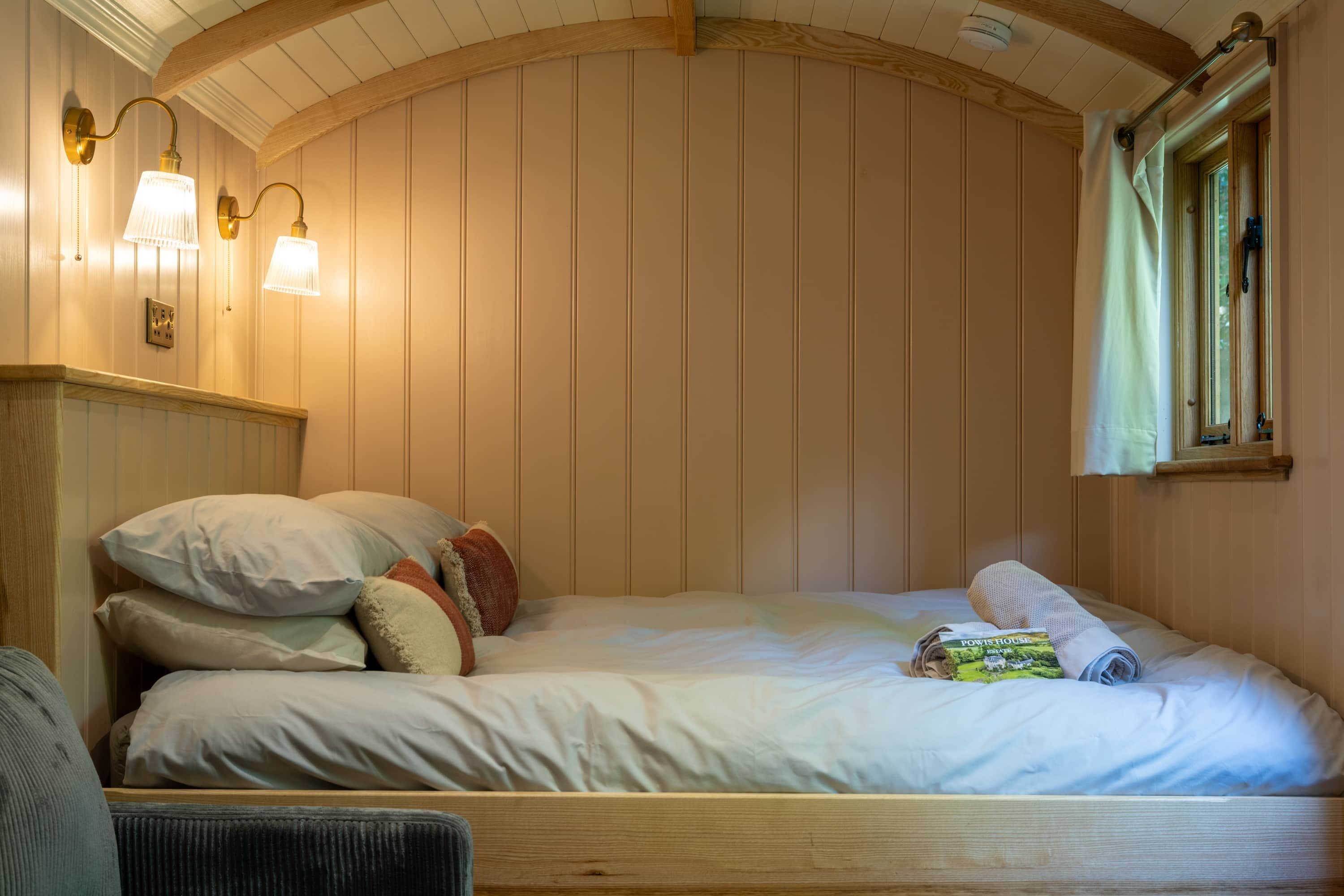 A bedroom with a wooden headboard, a bed with multiple pillows, a bedside table, and wall-mounted lamps.