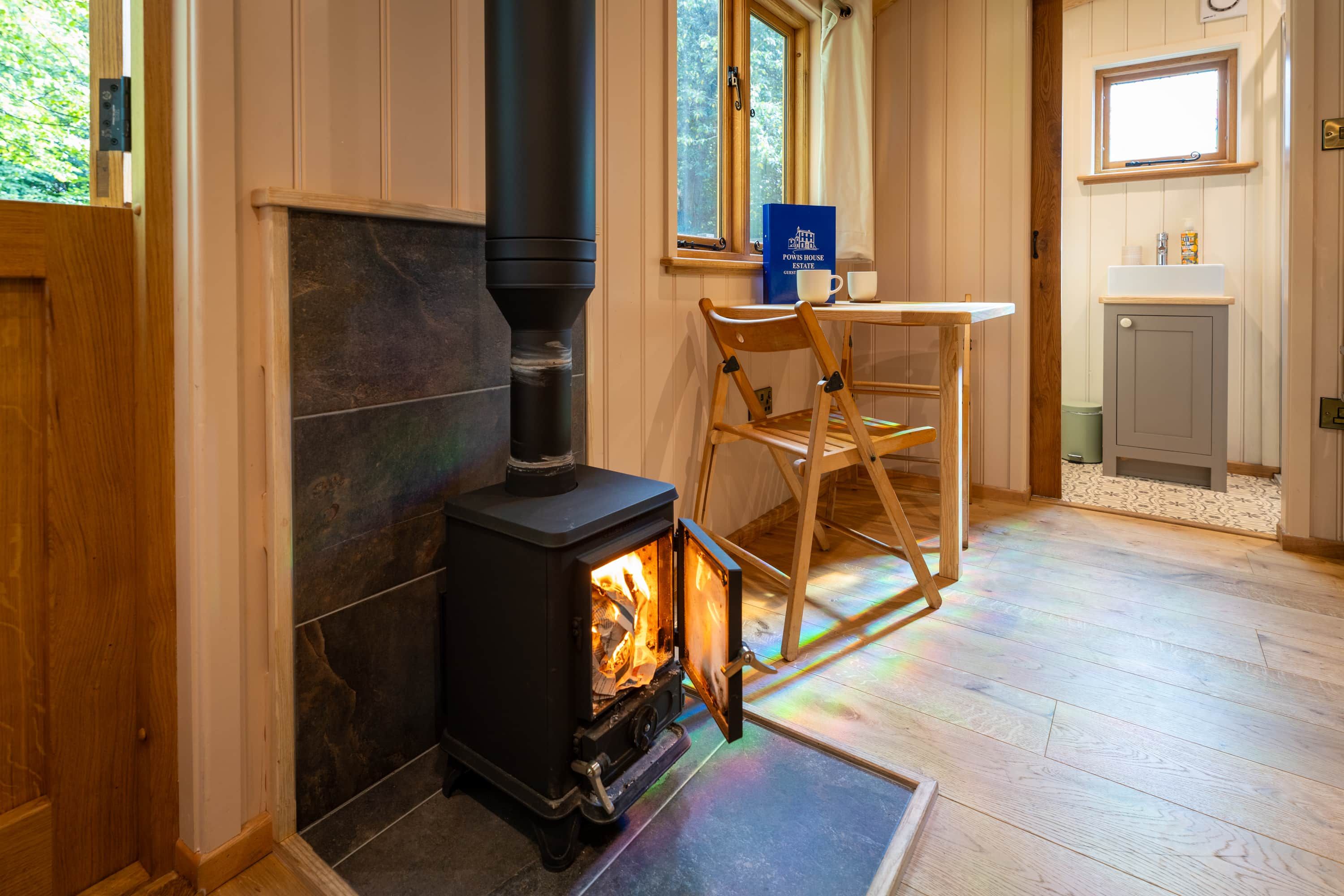 A cozy room with a wood-burning stove, a wooden chair, a table, and a window.