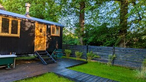 A rustic cabin with a wooden deck, a small outdoor seating area, and a wooden fence.