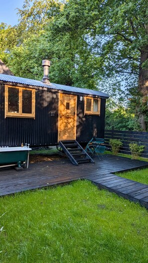 A small cabin with a metal roof, a wooden door, and a chimney. There is a small dock with a boat and a bench.
