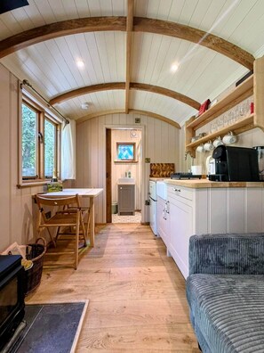 A cozy kitchen with wooden beams, a dining area with a table and chairs, and a view through a window.