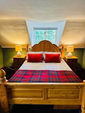 A bedroom with a wooden bed, red pillows, a plaid bedspread, two bedside lamps, and a window with a view of greenery. - Scottish Estate Getaway at Powis House Estate (Stirling)