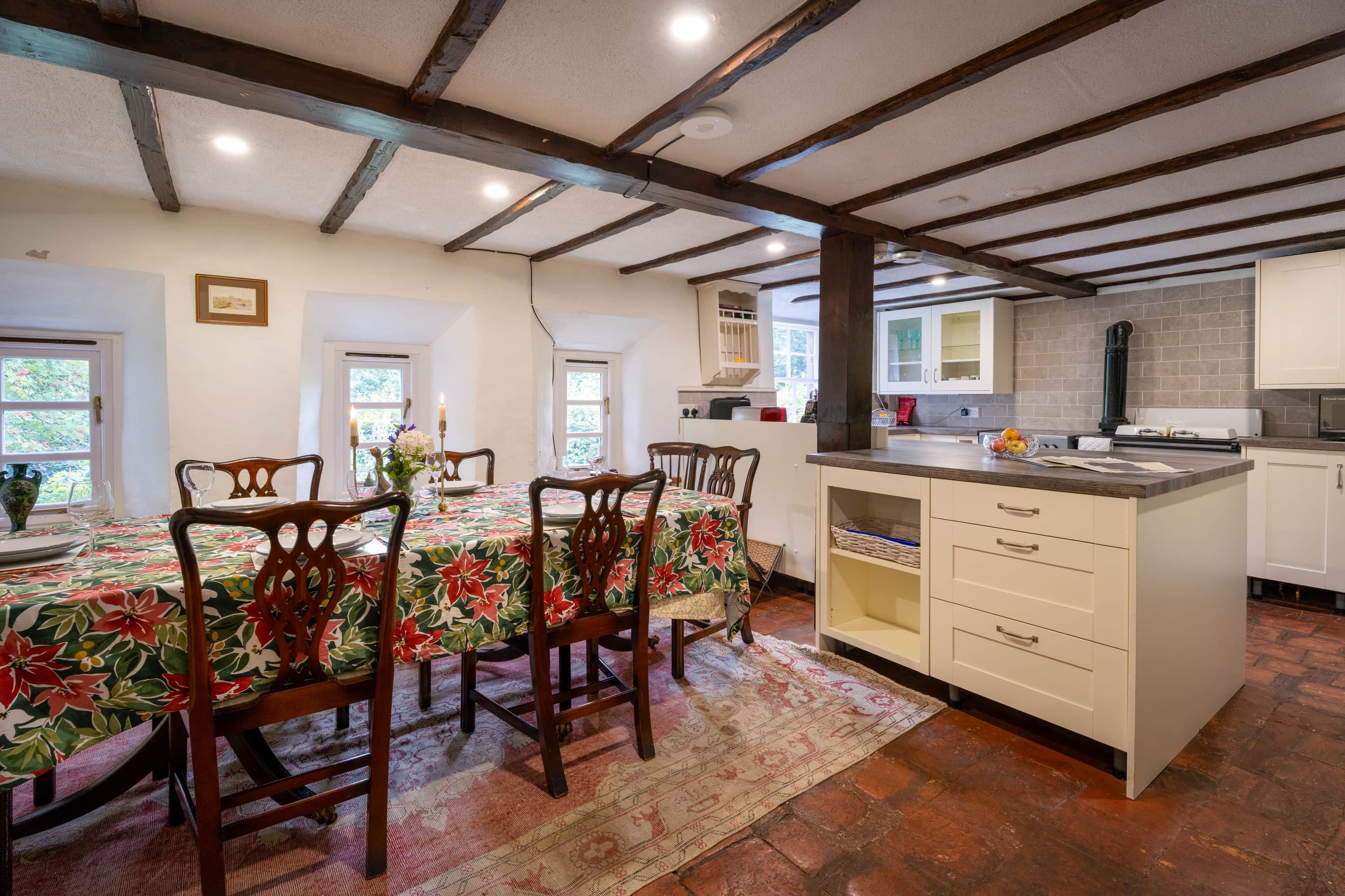 A dining area with a table set for four, wooden chairs, and a floral tablecloth.