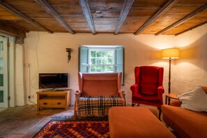 A cozy room with a wooden ceiling, a television on a wooden stand, a plaid chair, a red armchair, and a floor lamp. - Scottish Estate Getaway at Powis House Estate (Stirling)