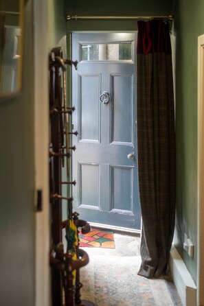Un couloir mène à une porte bleu foncé, dotée d’un trou de serrure et d’une poignée de porte. Un rideau est accroché sur le côté droit de la porte.