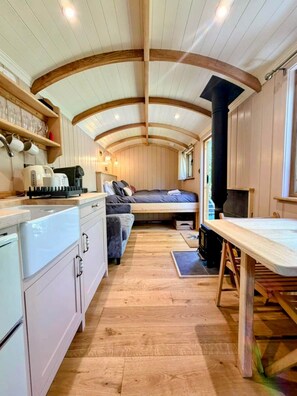 Un intérieur compact aux murs lambrés, comprenant un coin cuisine, un lit et un espace repas.