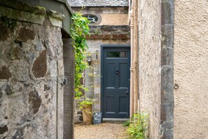 A narrow alleyway with a dark blue door, a stone wall, and a small garden area with a potted plant.