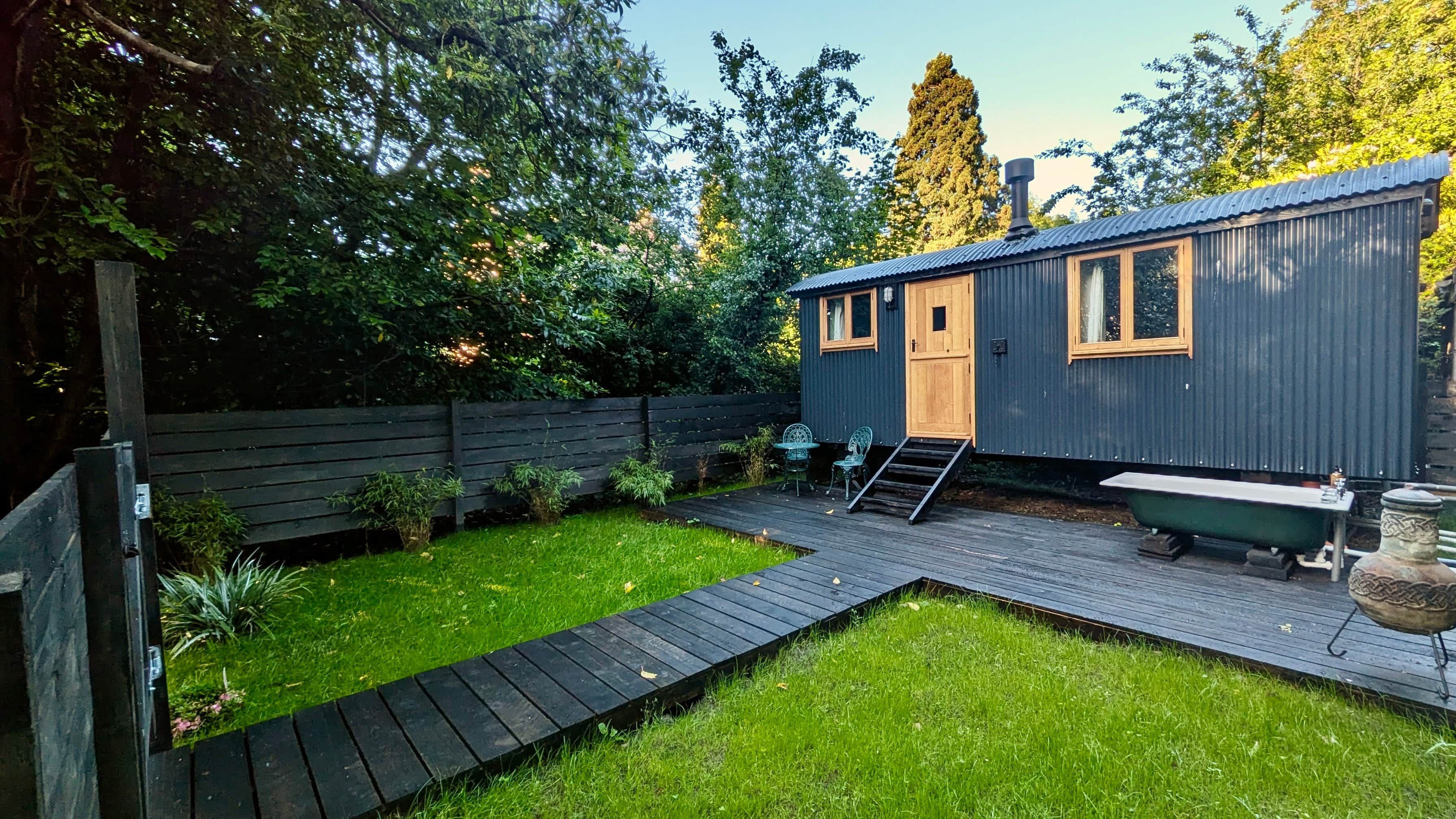 A small, single-story building with a wooden deck, a small outdoor seating area, and a grassy yard.