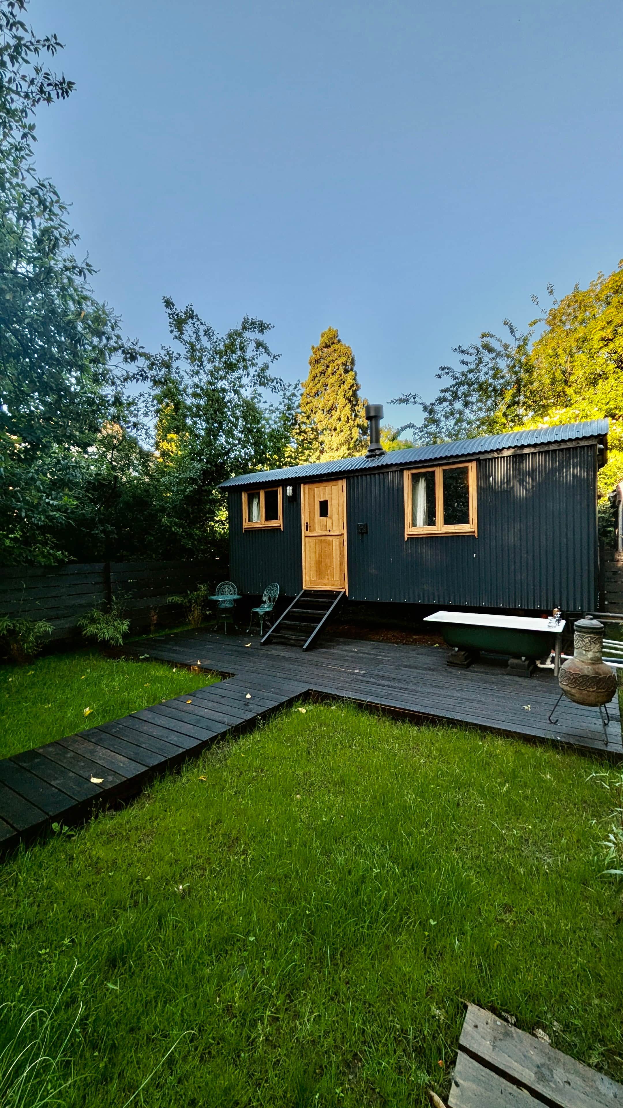 A small, single-story cabin with a wooden door and windows, a ramp leading to the entrance, and a small deck area.
