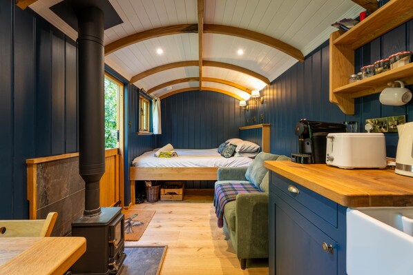 Une pièce compacte et accueillante, comprenant un lit, une petite kitchenette et une table en bois.