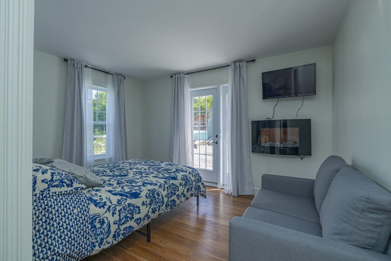 A bedroom with a bed, a gray sofa, a TV, and a window with curtains.