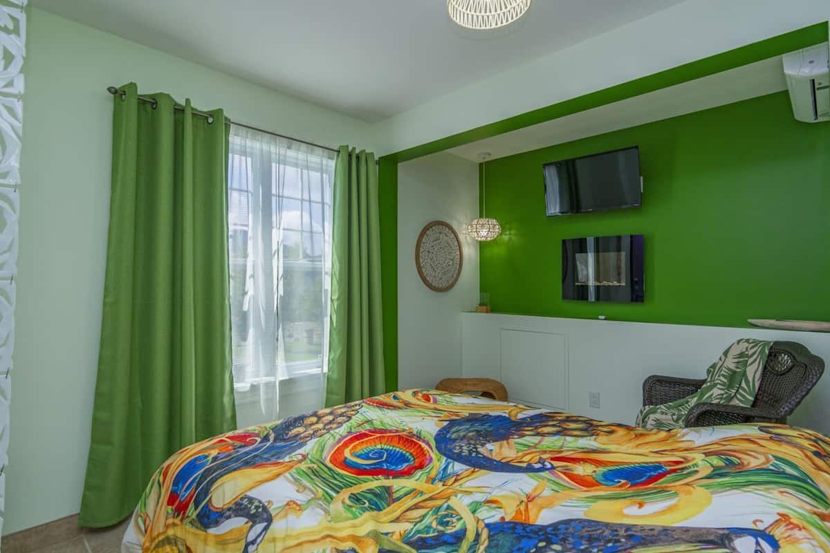 A room with a bed, green curtains, a television, and a wall-mounted air conditioner.