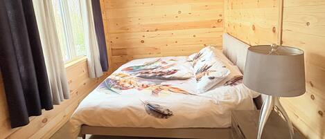 Une chambre dans un chalet en bois, avec un lit, une table de chevet et une fenêtre avec des rideaux.