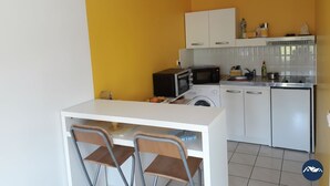 Une cuisine compacte avec un plan de travail blanc, deux chaises, un four à micro-ondes, un lave-linge et un évier.