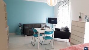 Une pièce de taille modeste avec un mur bleu, une table blanche avec des chaises, un canapé gris, un téléviseur et une armoire.