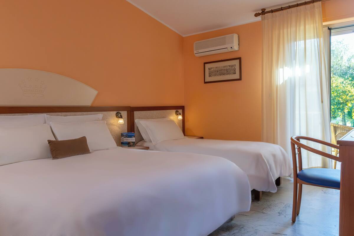 Une chambre d’hôtel avec deux lits, une chaise, un appareil de climatisation et une fenêtre avec des rideaux.
