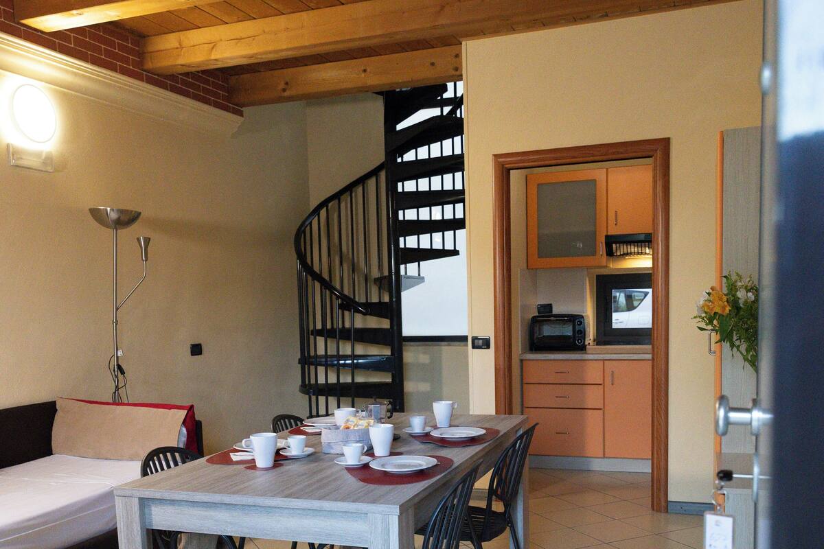 Un espace repas avec une table et des chaises en bois, un escalier en colimaçon et une cuisine en arrière-plan.