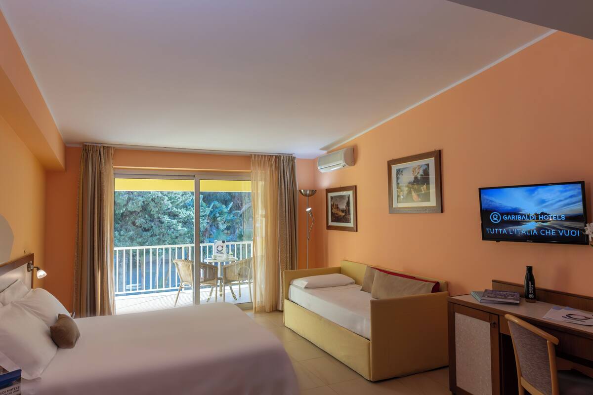 Une chambre d’hôtel comprenant un lit, un canapé, un bureau, une télévision et un balcon avec vue sur les arbres.