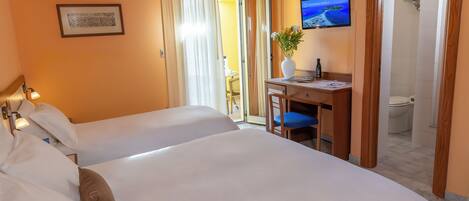 Habitación de hotel con dos camas, un escritorio con silla, televisión y baño a la vista a través de una puerta abierta.
