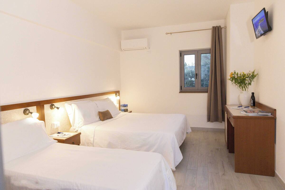 Une chambre d’hôtel avec deux lits, un bureau, une télévision et une fenêtre avec des rideaux.