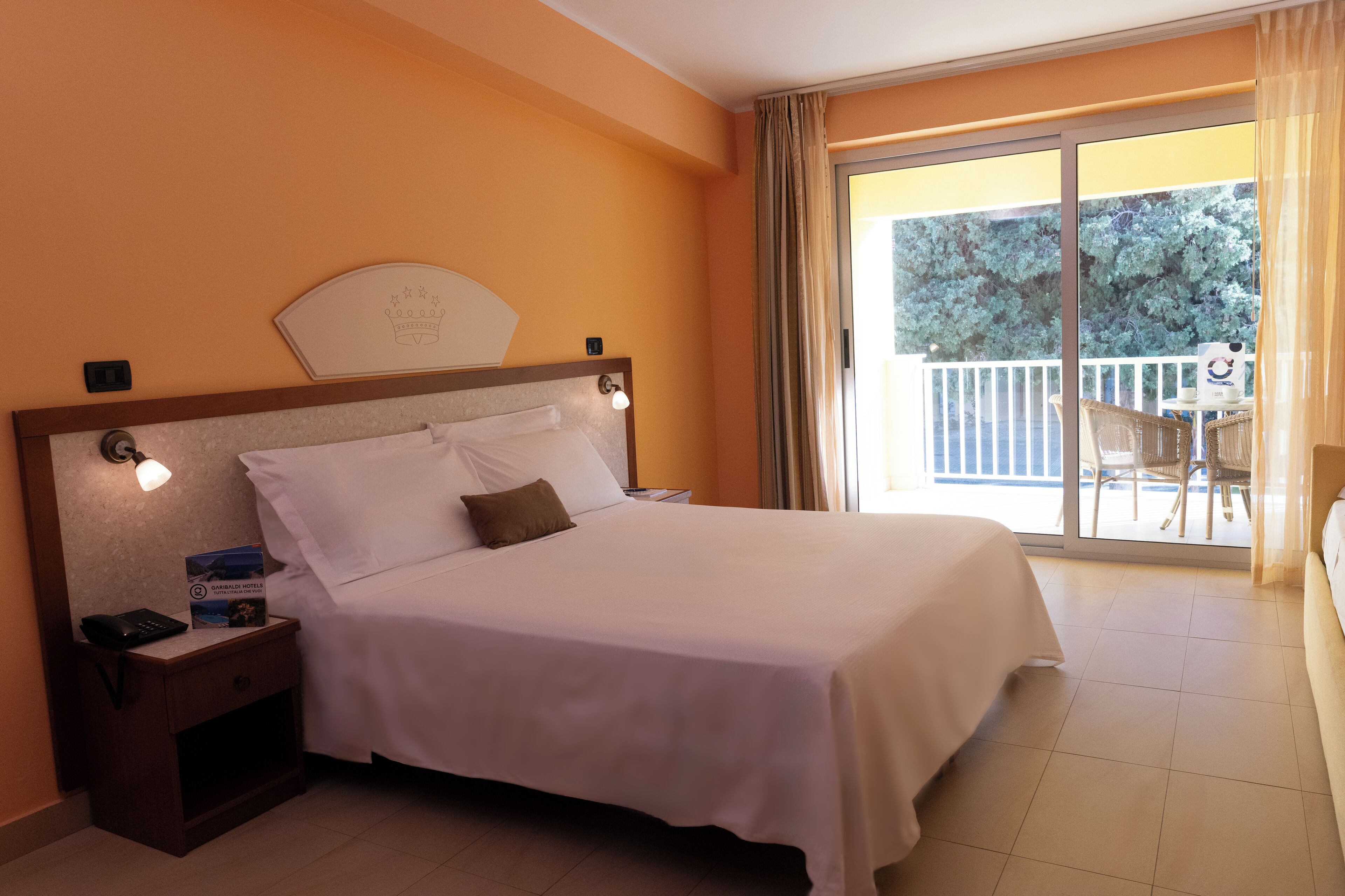 Habitación de hotel con cama, mesita de noche, ventana con cortinas y vista al balcón exterior.