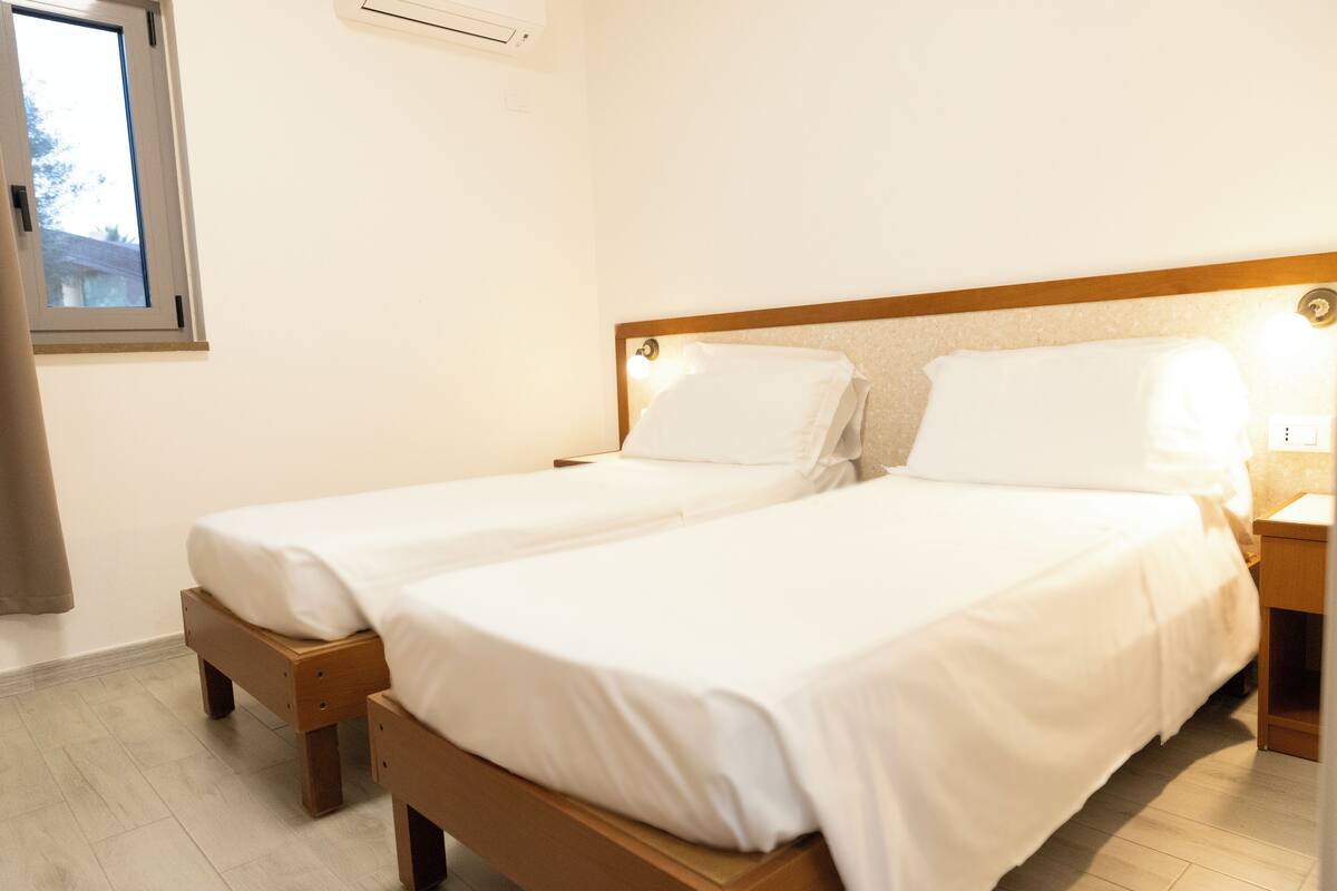 Un lit double avec une tête de lit en bois et du linge de lit blanc, dans une chambre d’hôtel.