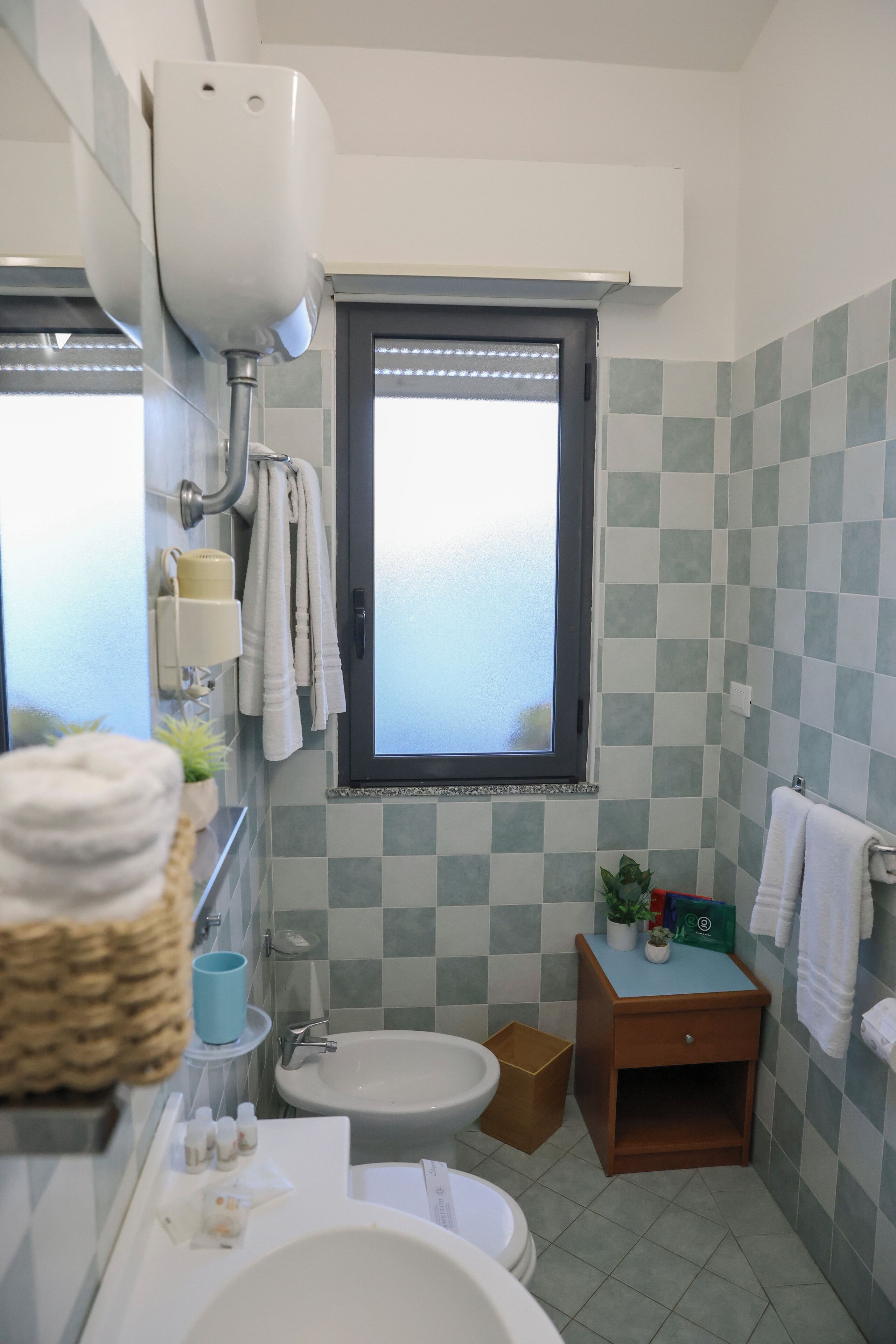 A bathroom with a sink, mirror, towel rack, window, and a small wooden cabinet.
