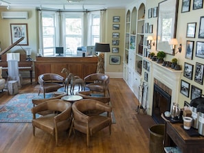 Un vaste salon agrémenté d’un piano, de fauteuils en cuir, d’une cheminée et d’un mur décoré de tableaux encadrés.