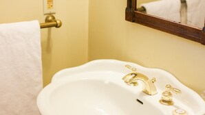 A bathroom with a white sink, gold faucets, and a mirror.
