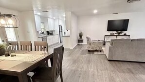 Ein modernes Wohnzimmer mit Essbereich, einer dahinterliegenden Küche und einem an der Wand befestigten Flachbildfernseher.