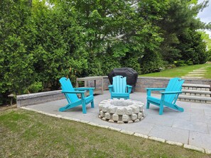 A patio with three turquoise Adirondack chairs, a stone fire pit, and a black grill cover. - Irene's Hideaway (Tisbury)