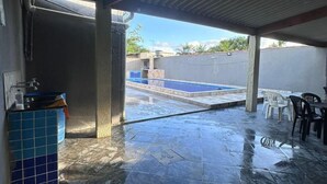 An open patio with a tiled floor, a blue water dispenser, and a covered area with chairs and tables.