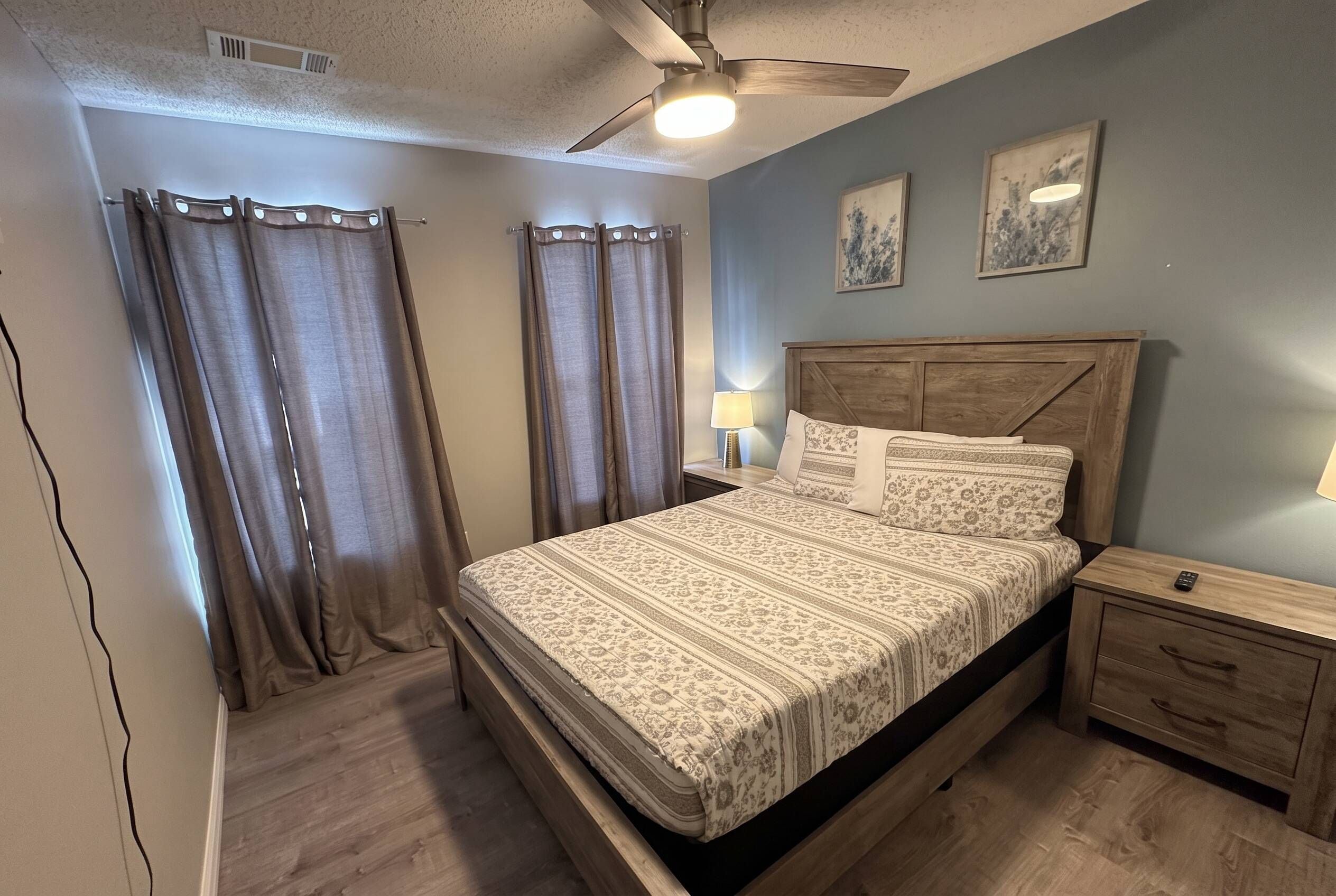 A bedroom with a bed, nightstands, a ceiling fan, and curtains.