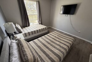 Ein Schlafzimmer mit zwei Betten, einem an der Wand befestigten Fernseher und einem Fenster mit Vorhängen.