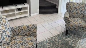 Een woonkamer met gestreept banken, een flatscreen televisie op een witte standaard, een trap en uitzicht op het buitengebied.
