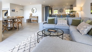 A modern living room with a sofa, coffee table, and dining area with chairs and a table. - Mill Village 71/72, Milly Cottage - Lakeside, Onsite Facilities, Pool, Sleeps 11 (Somerford Keynes)