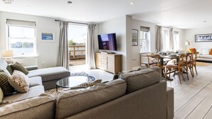A modern living room with a sofa, coffee table, TV, and dining area with chairs and a table. - Mill Village 71/72, Milly Cottage - Lakeside, Onsite Facilities, Pool, Sleeps 11 (Somerford Keynes)