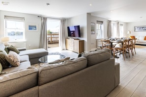 Una sala de estar moderna con sofá, mesa de centro, televisor y comedor con sillas y una mesa.