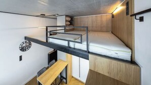 Une chambre compacte et moderne, équipée d’un lit superposé, d’un petit bureau et d’une horloge murale.