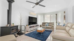 A modern living room with a fireplace, sofa, TV, and a ceiling fan. - Casa LuCe by Experience Jervis Bay (Old Erowal Bay)