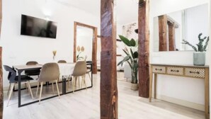 Un'area pranzo moderna con un tavolo e sedie in legno, una TV a schermo piatto montata a parete e un grande specchio sopra un tavolo consolle.