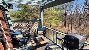 A wooden deck with a grill, outdoor seating, and a view of trees.